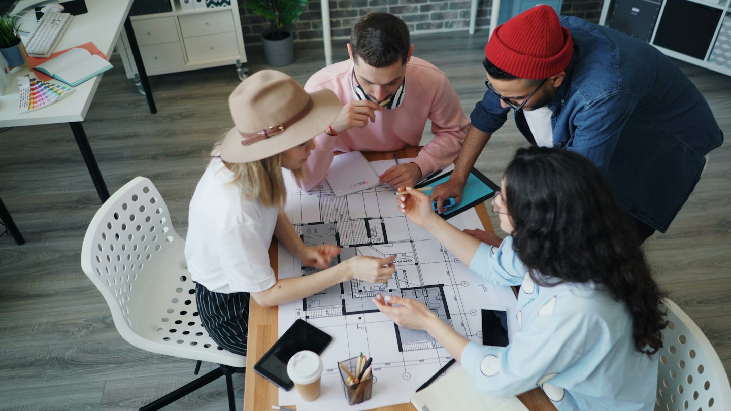 Equipo diverso colabora en planos arquitectónicos en una oficina moderna.