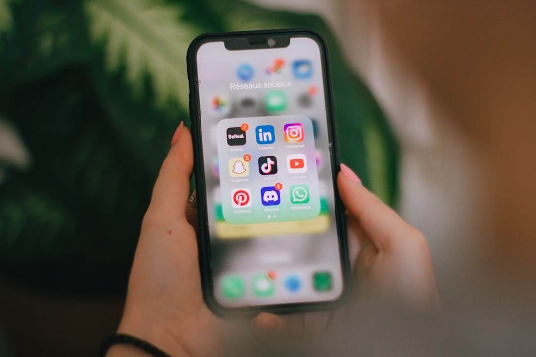 Person holding iPhone showing social media app icons.